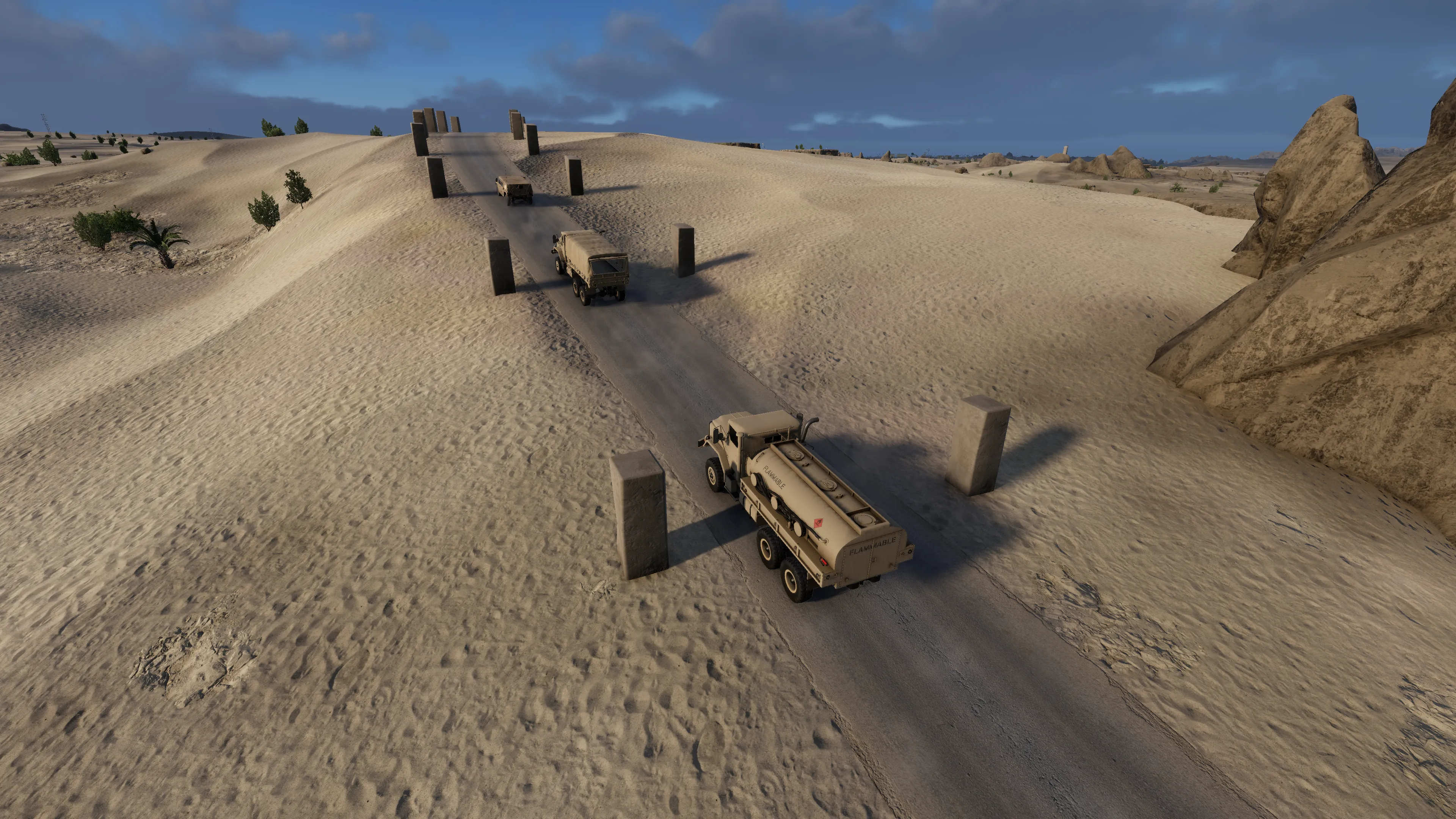A convoy of two large trucks and a humvee through a desert.